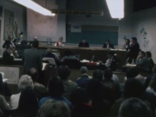 Film still from the 1974 Huntington Beach council meeting: the chamber seen from the audience, council at the dais