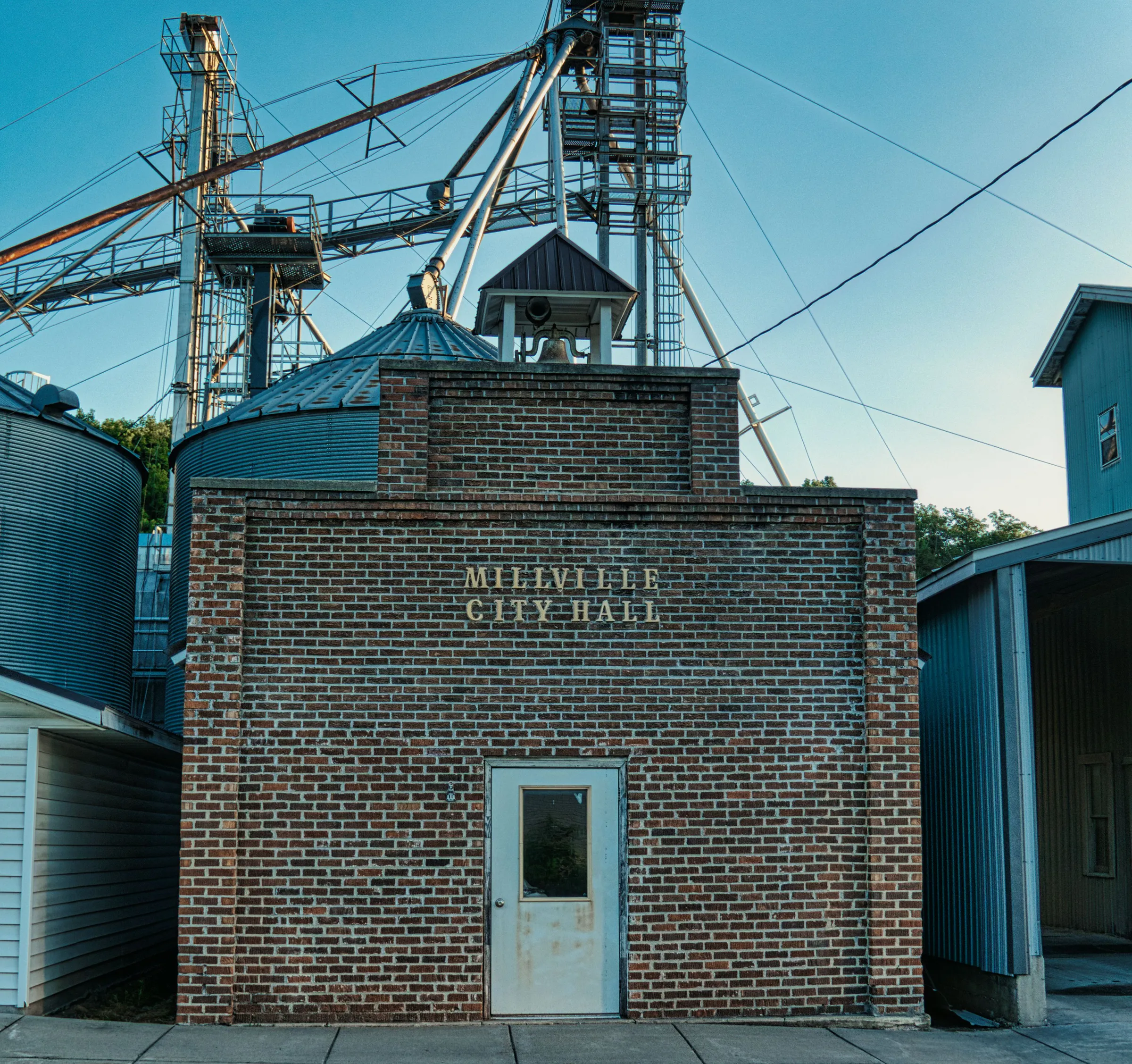 Millville City Hall: a one-story brick building with a single door, grain elevators behind it